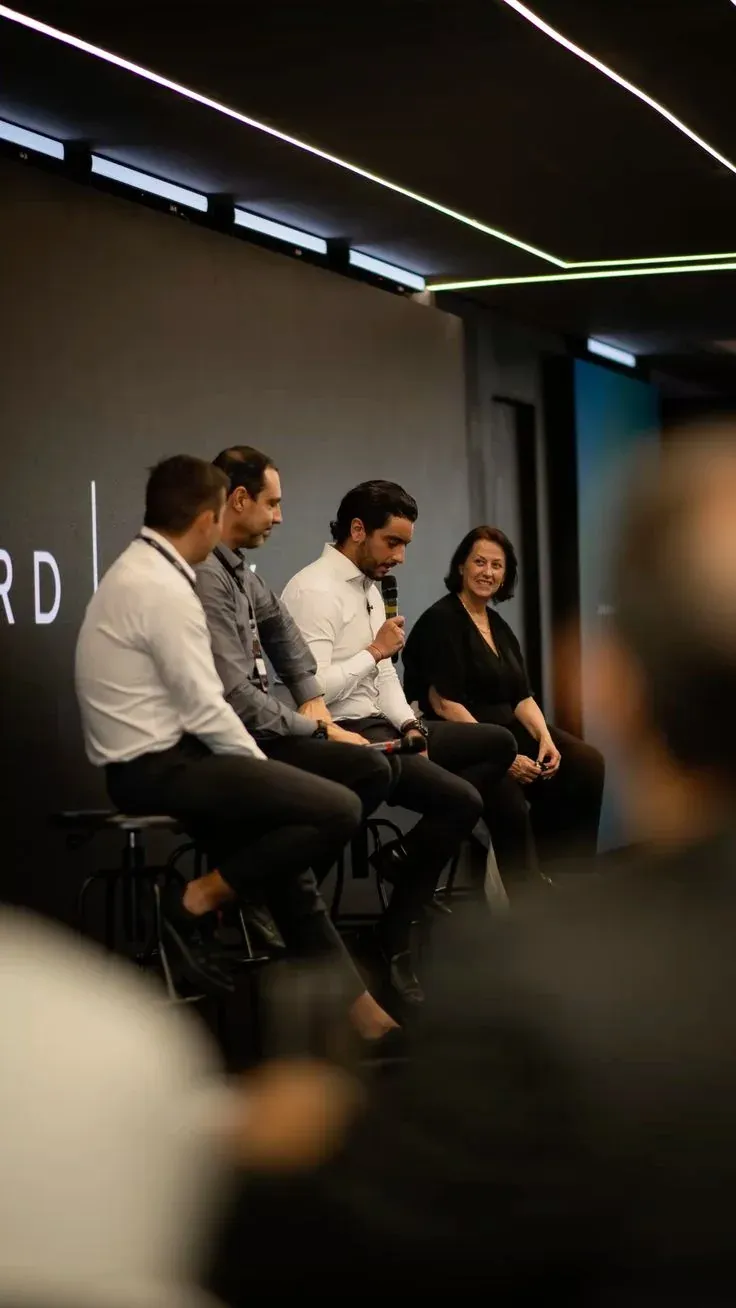 Table ronde devant un grand écran sombre : quatre intervenants sur de hauts tabourets, l’un parle au micro sans fil, une intervenante sourit