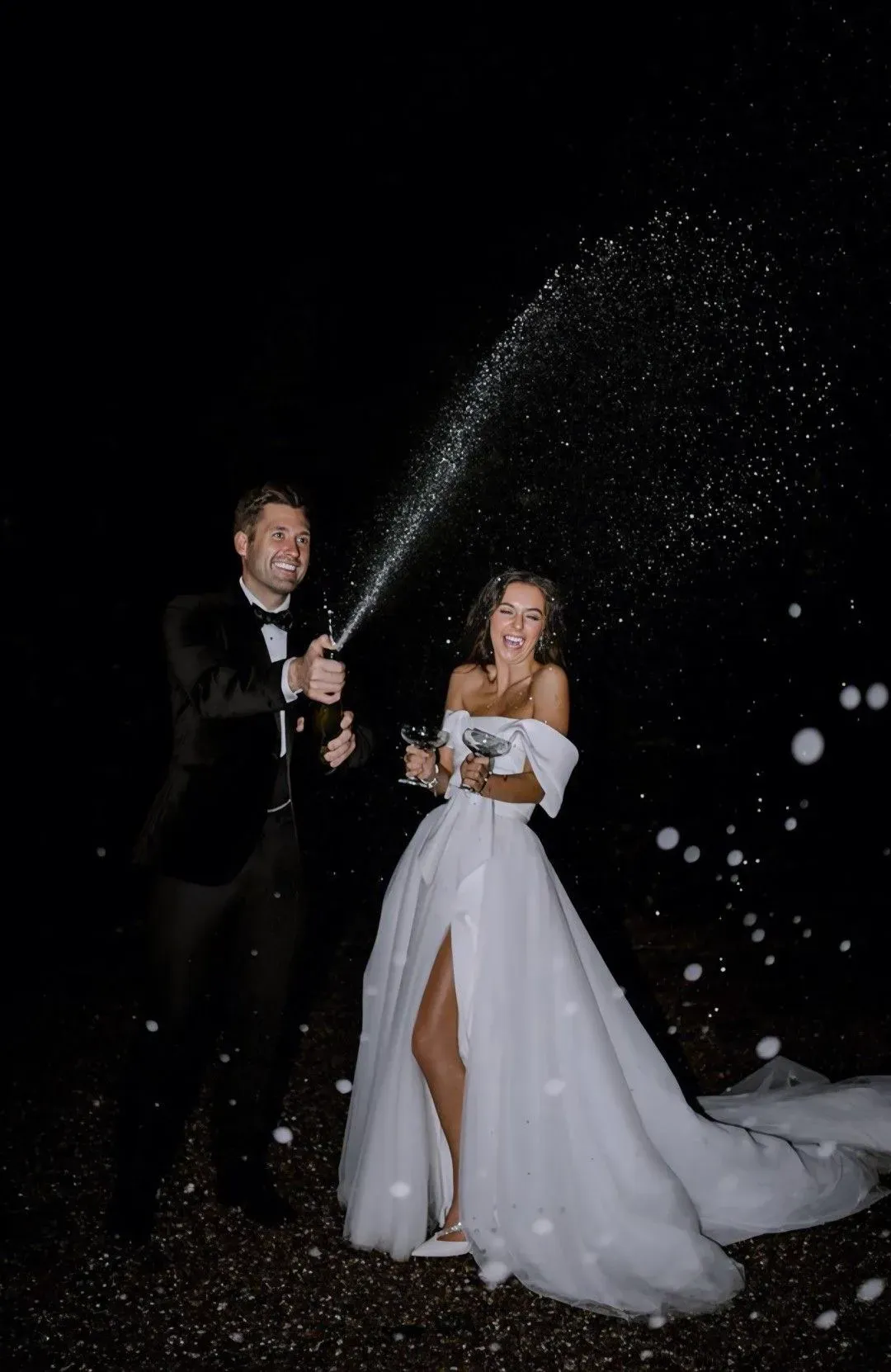 Des mariés en costume noir et robe blanche font jaillir le champagne, de nuit