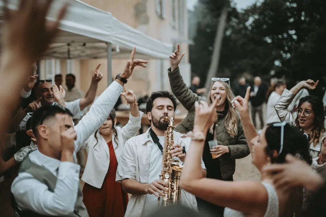 Le saxophoniste Malo Despré joue au milieu des invités qui dansent bras levés, devant une tente blanche et la façade d’une maison.